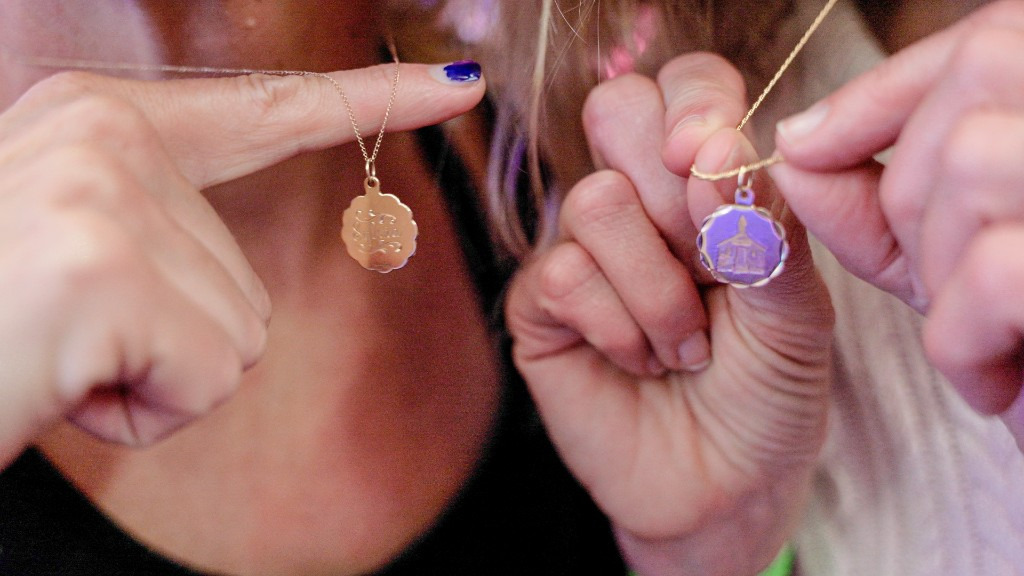 Sylvia Wolff and Meghan Agresto both hold up matching necklaces engraved with their names and the historic schoolhouse. A symbol of their accomplishments and friendship.