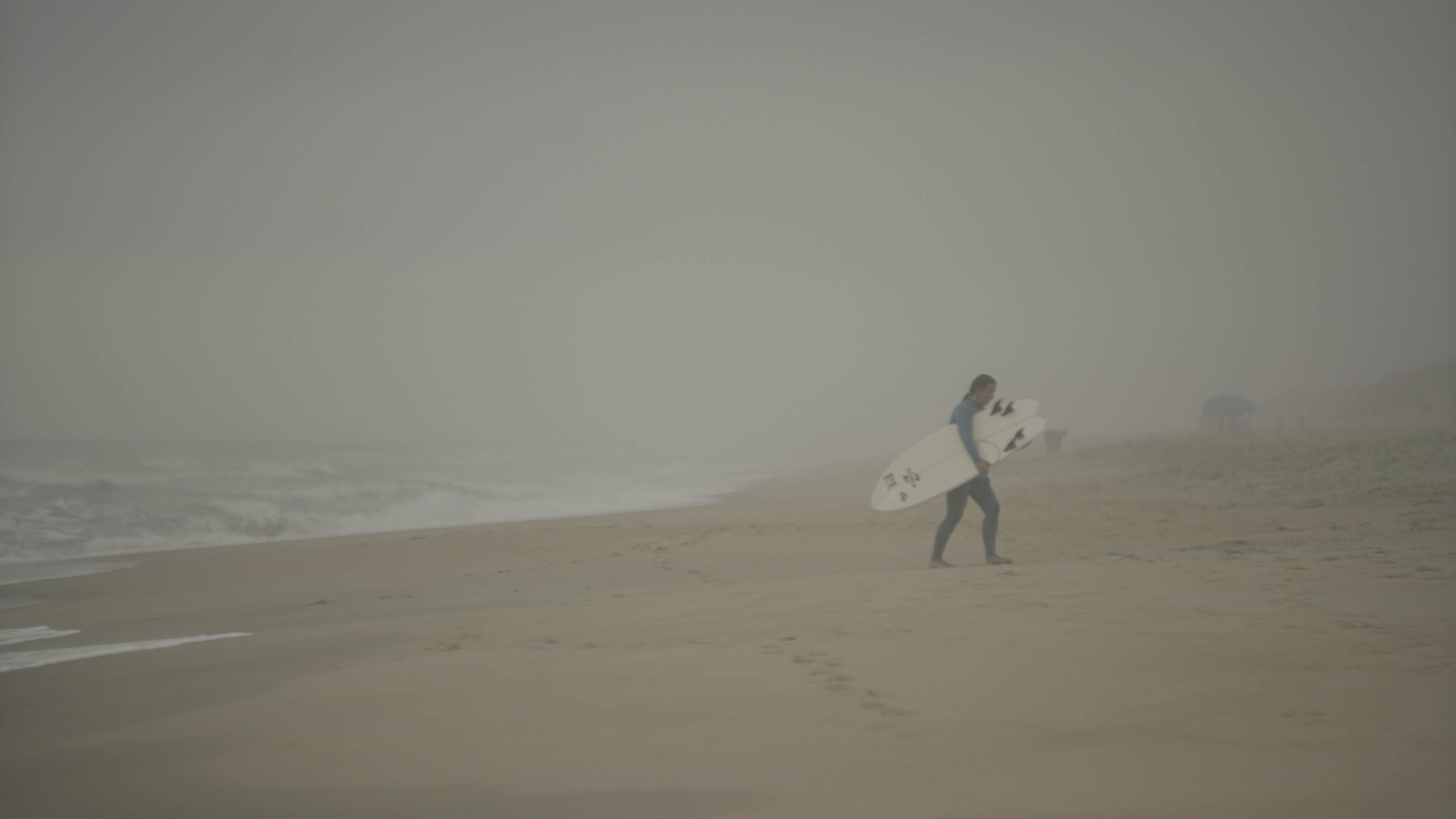 Female surfer holding surfboard walks away from beach.