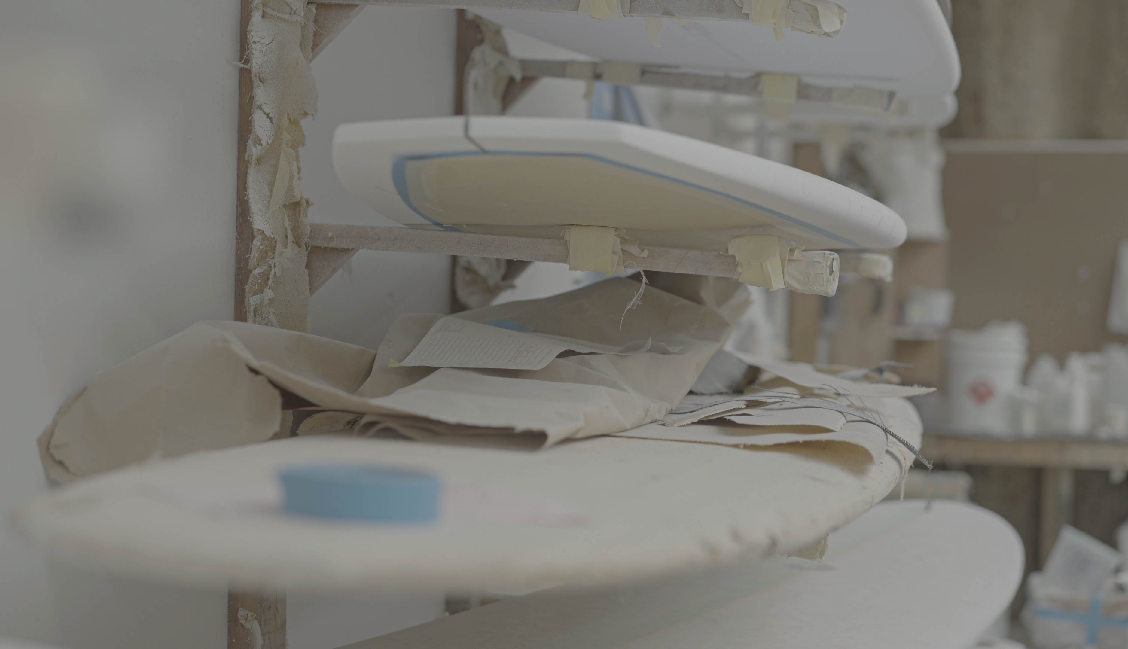 Sand paper sits on top of uncarved surfboards in a workshop.